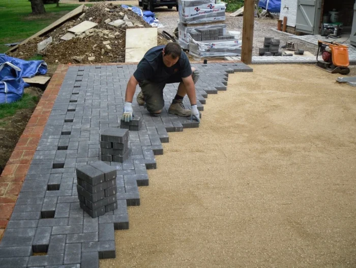 Pekerja memasang paving block di atas hamparan pasir untuk area halaman rumah