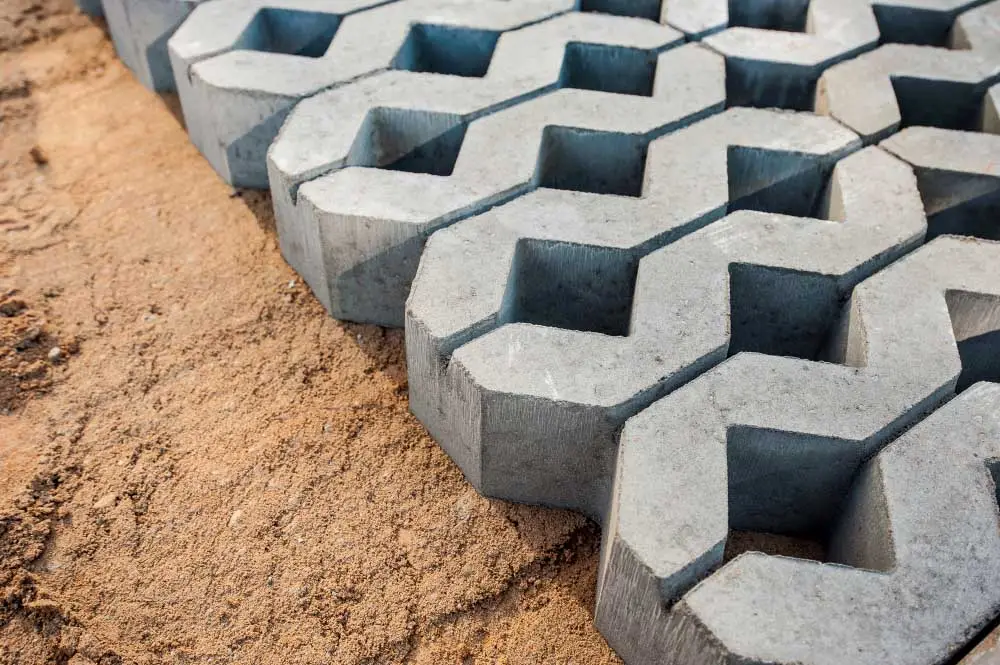 Paving Solo Raya motif grass block berwarna abu-abu di atas hamparan pasir saat proses pemasangan.
