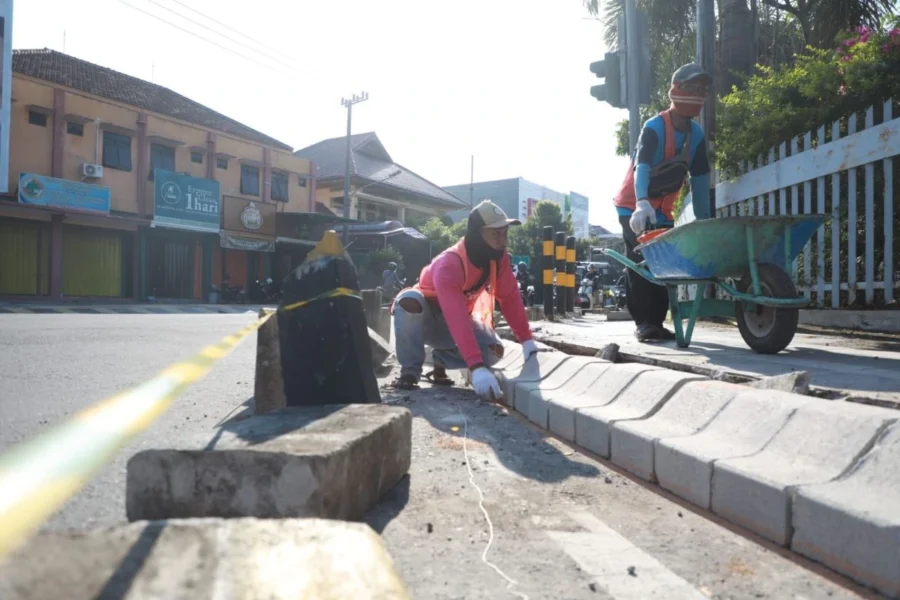 Pekerja memasang kanstin beton di tepi jalan kota untuk proyek perbaikan trotoar dan drainase jalan raya.