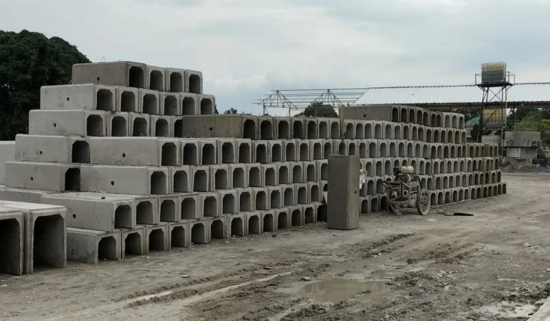 Tumpukan U Ditch beton pracetak berbagai ukuran di area pabrik produksi beton.