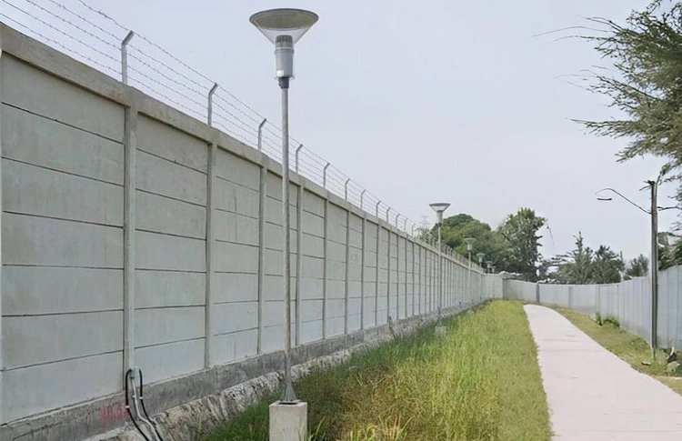 Pagar panel beton tinggi dengan kawat duri terpasang di area fasilitas umum dan jalan setapak