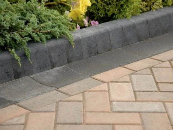 Potongan kanstin beton warna abu-abu sebagai pembatas taman dengan paving block motif anyam berwarna krem dan abu-abu.
