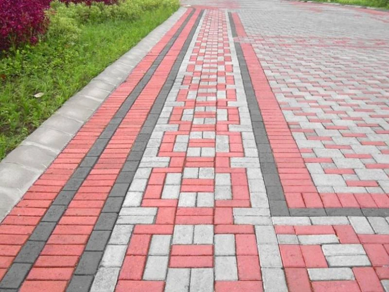 Kombinasi paving block merah abu hitam dengan pola hias geometris di area pedestrian taman