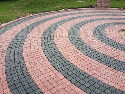 Paving block motif lingkaran dengan kombinasi warna merah dan abu-abu tersusun rapi di area taman.