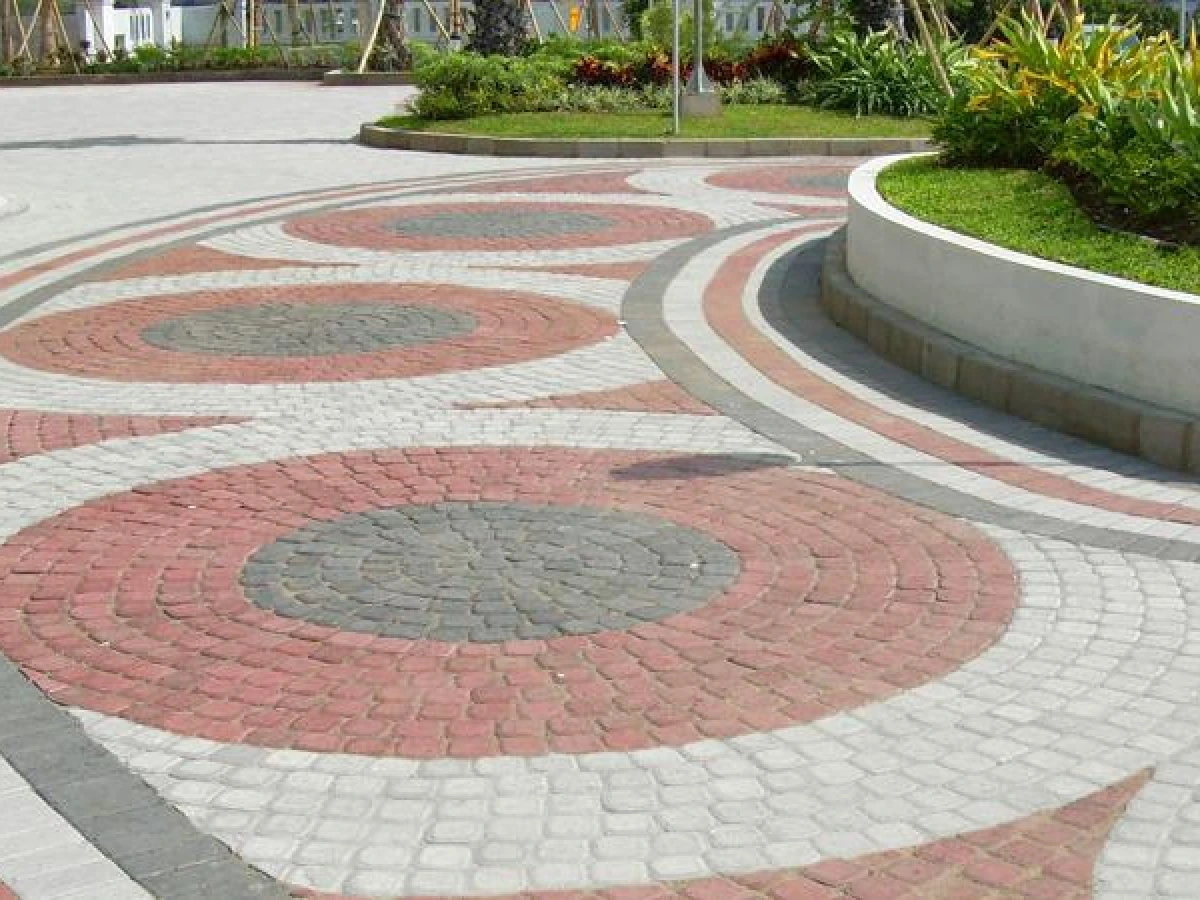 Desain paving block motif lingkaran berwarna merah, abu-abu, dan putih di area taman modern.