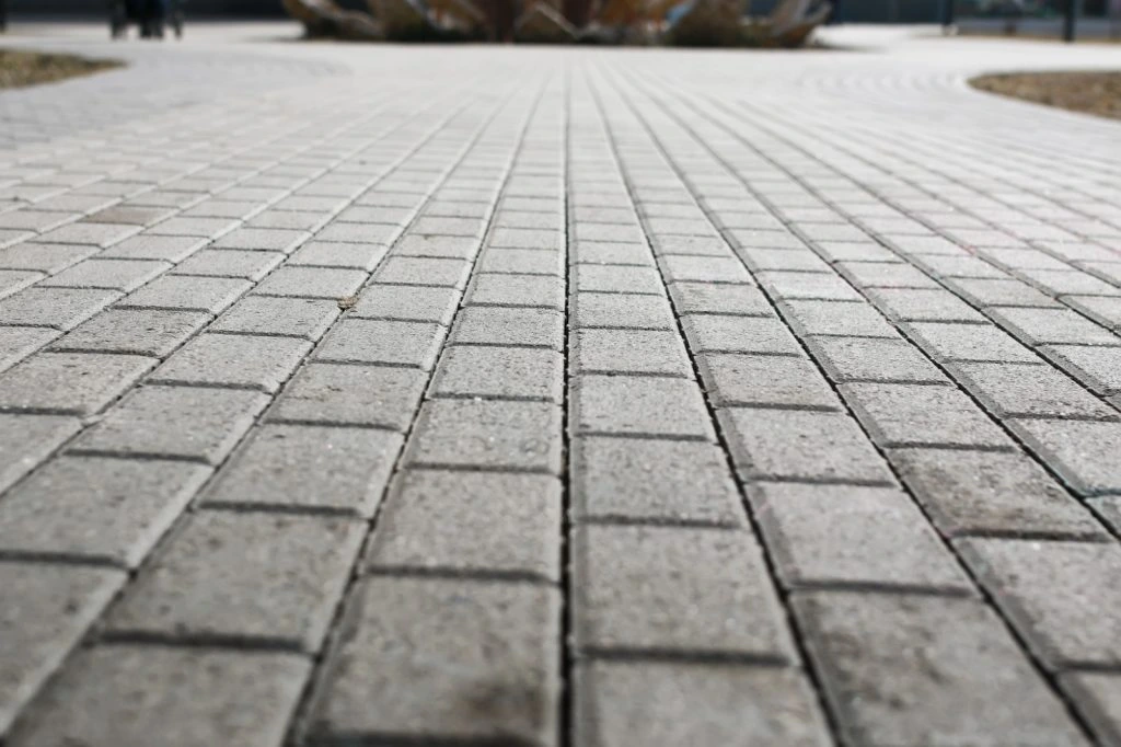 Permukaan paving block warna abu-abu yang tersusun rapi pada area jalan atau trotoar dengan pola persegi panjang.
