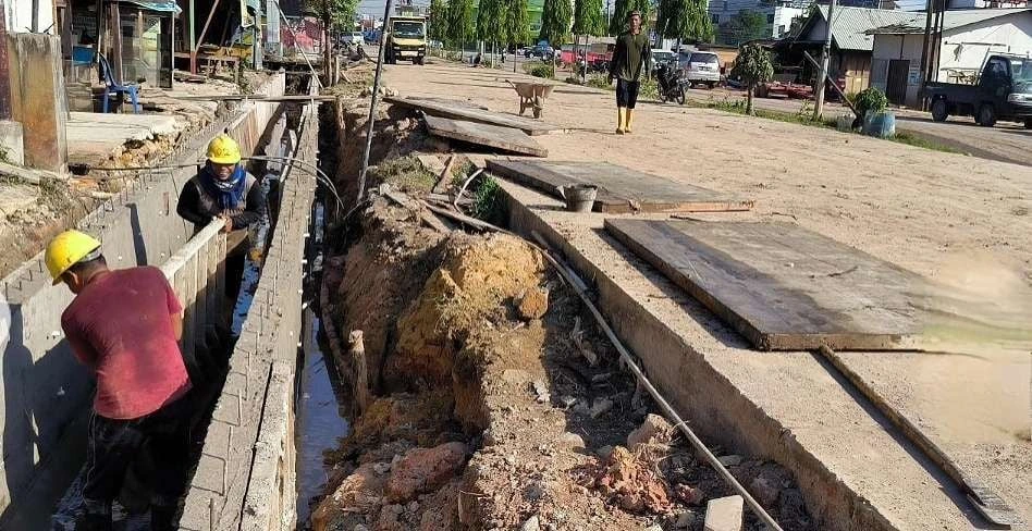 Pekerja konstruksi sedang membangun saluran drainase beton di area galian panjang pada proyek perbaikan infrastruktur.