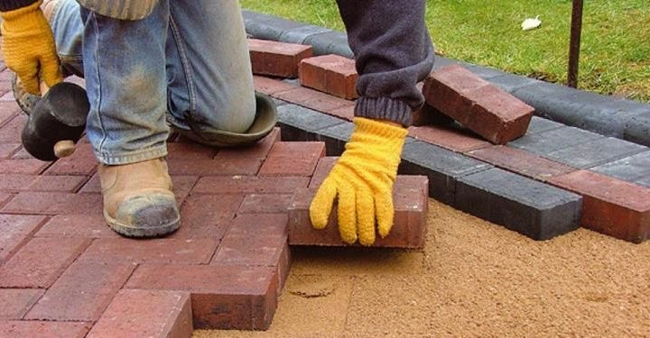 Tukang memasang paving block bata merah di atas lapisan pasir menggunakan sarung tangan kerja.